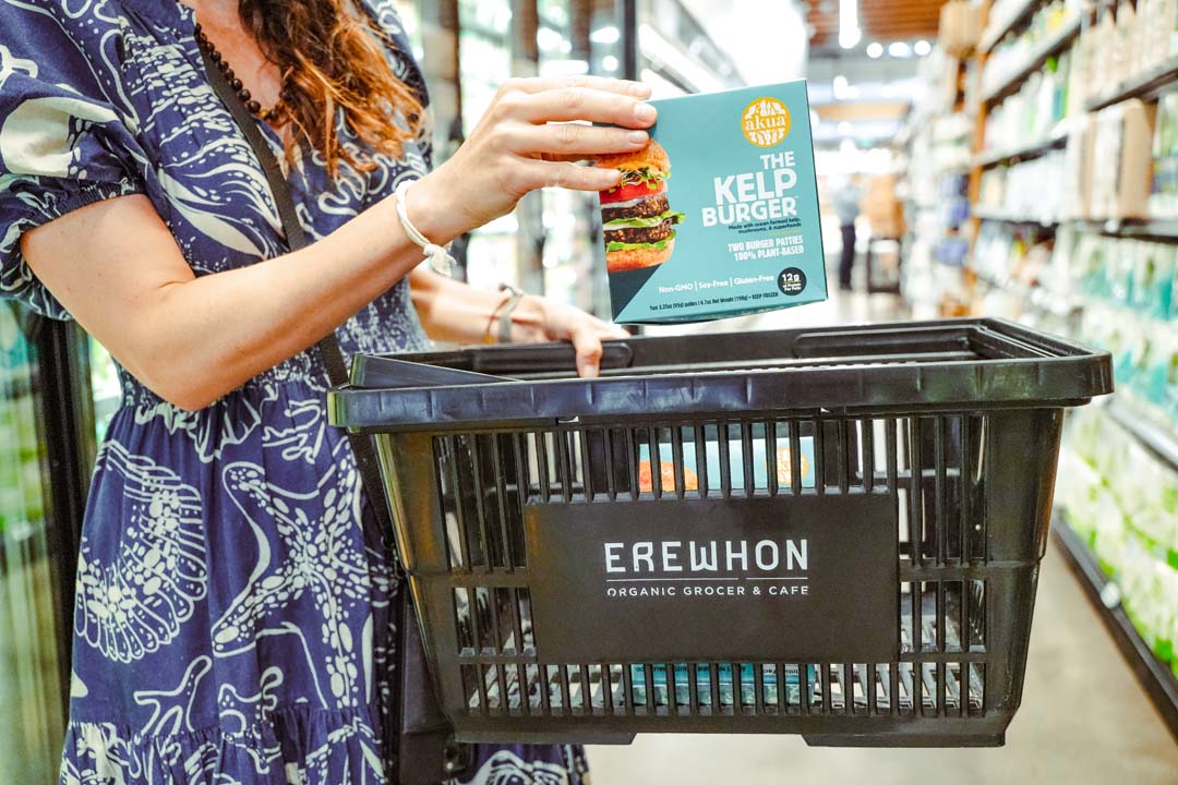 Someone placing a box of Akua's kelp burgers in an Erewhon grocery basket