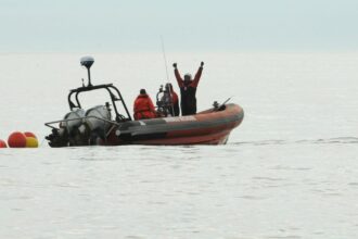 Man with arms outstretched overhead in a small boat with two people