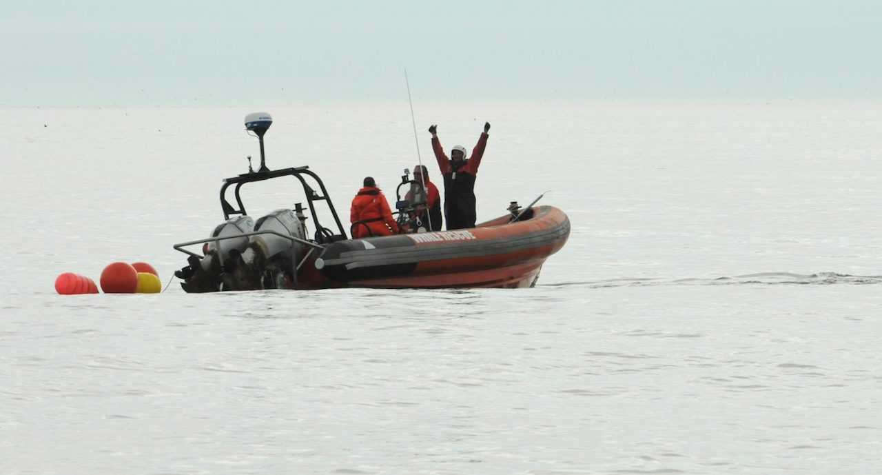 Man with arms outstretched overhead in a small boat with two people