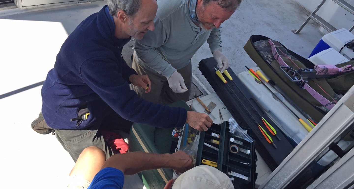Three men reaching for tools in a toolbox