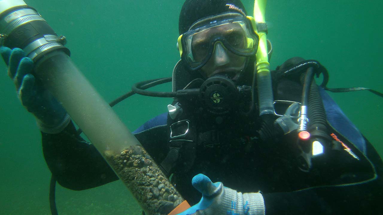 A scuba diver holding a tube of collected sediment to measure sequestered carbon