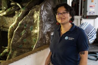 A person in a blue Aquarium shirt standing beside a tank