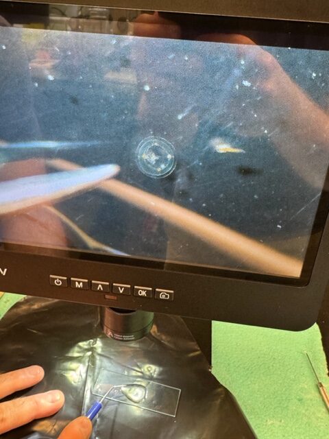 A digital screen shows a magnified circular object with instruments nearby.