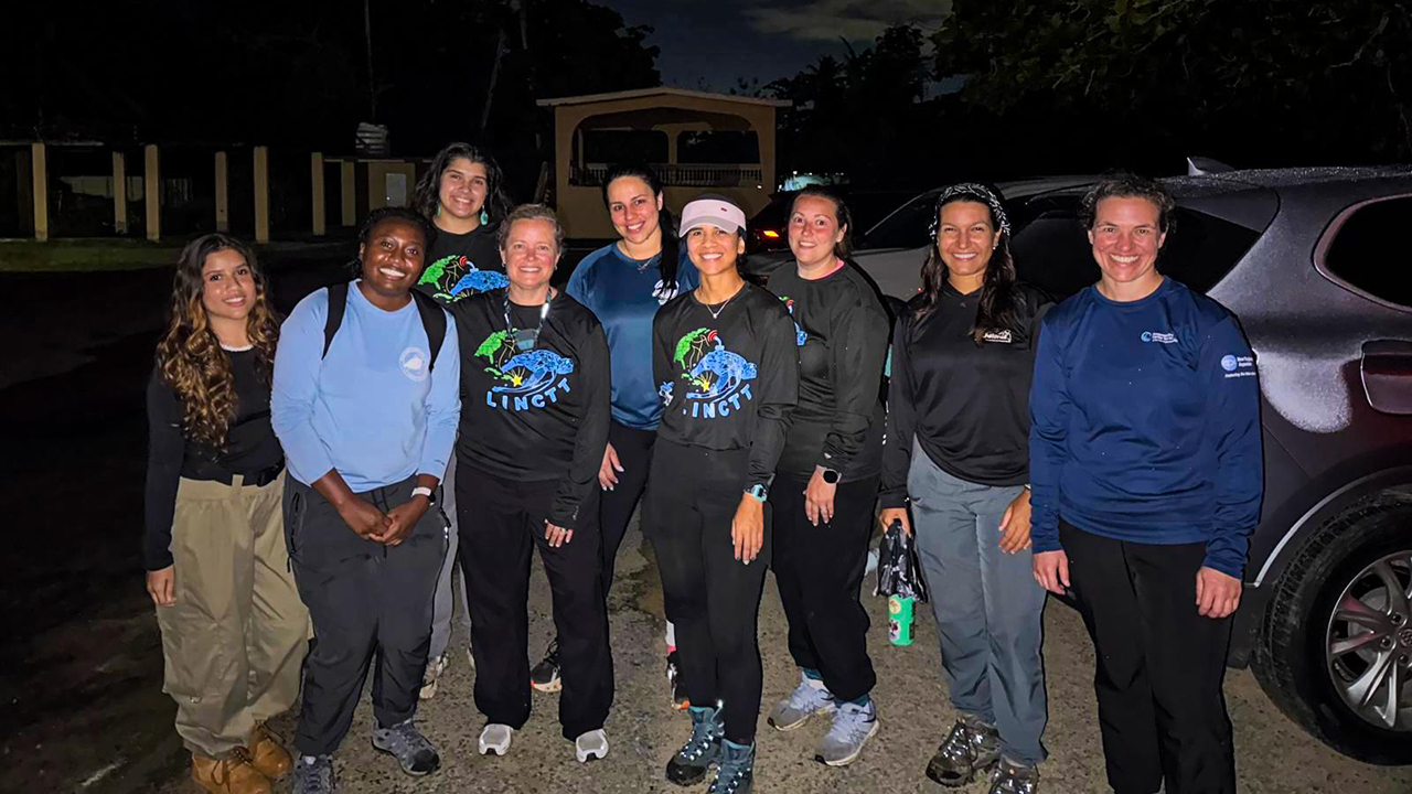 A group of nine people smiling outdoors at night.