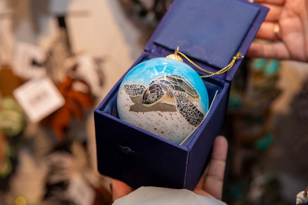 A glass globe ornament in a box, featuring a painting of a sea turtle