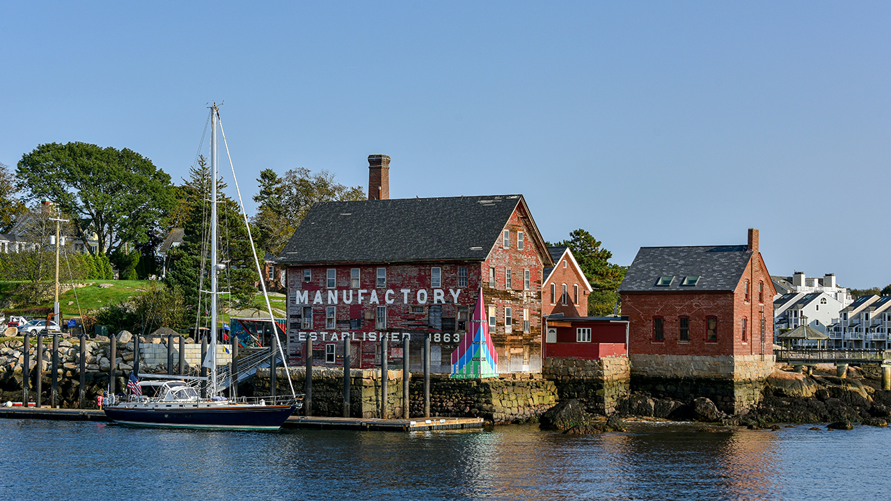 Waterfront with a historic red building and a sailboat moored nearby.