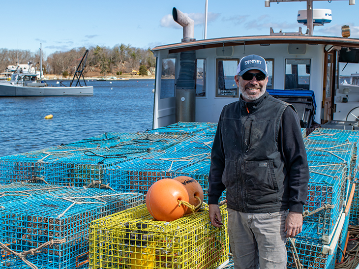 A fisher standing beside lobster gear on a fishing boat and smiling