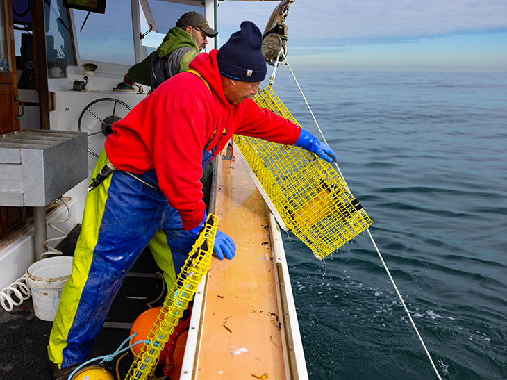 A fisher setting a ropeless lobster trap off the side of a boat