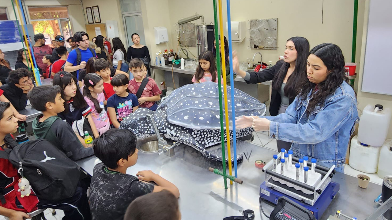 Two people presenting a model of a leatherback sea turtle in a classroom full of children