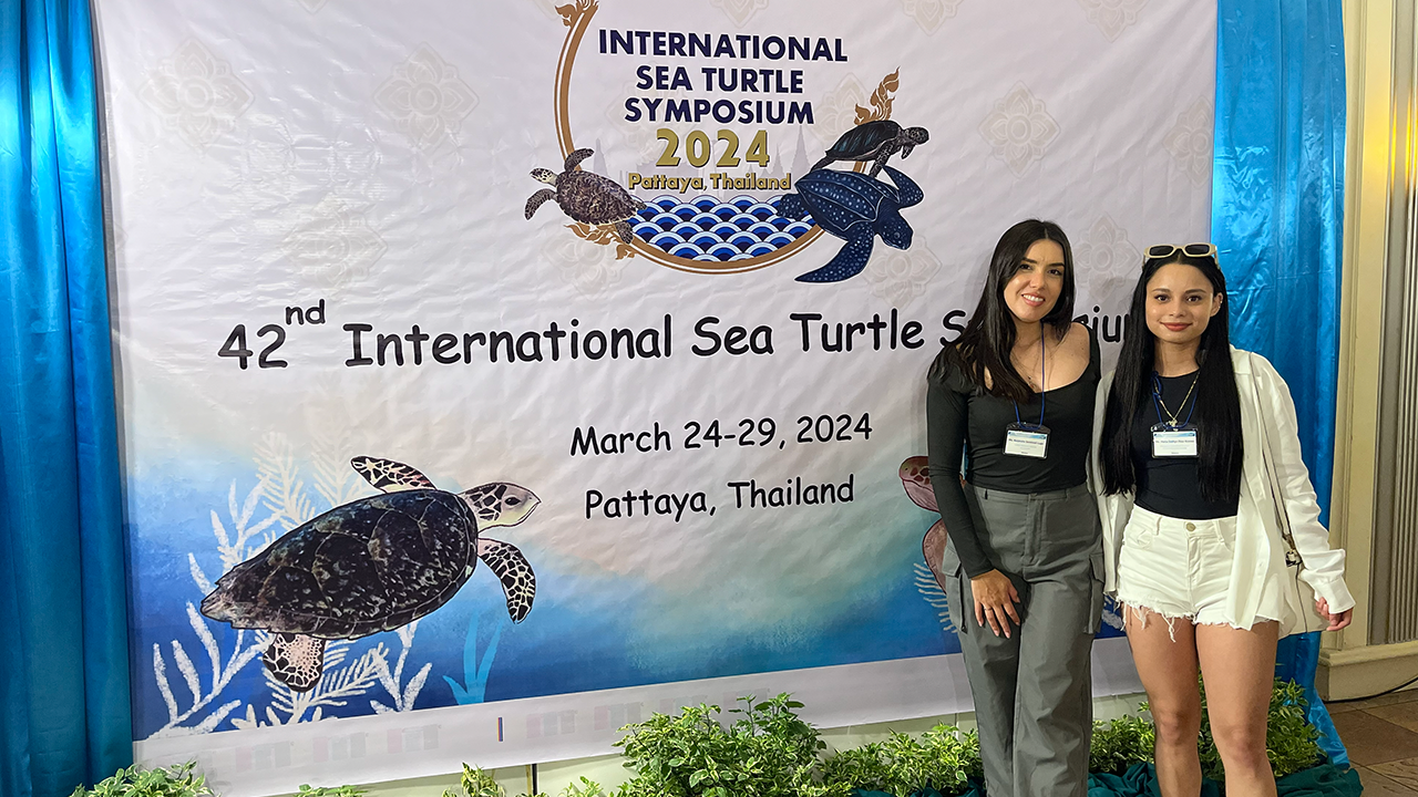 Two people posing in front of a banner for a sea turtle conference