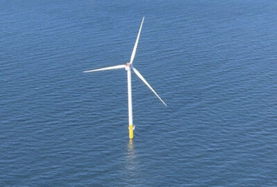 Offshore wind turbine with three white blades and a yellow base standing in blue water.
