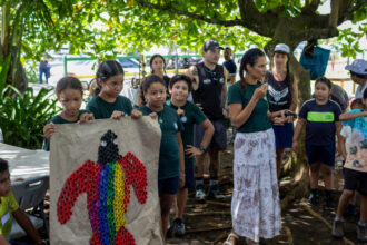 A community gathering with children holding a poster displaying a sea turtle made out of colorful bottle caps.